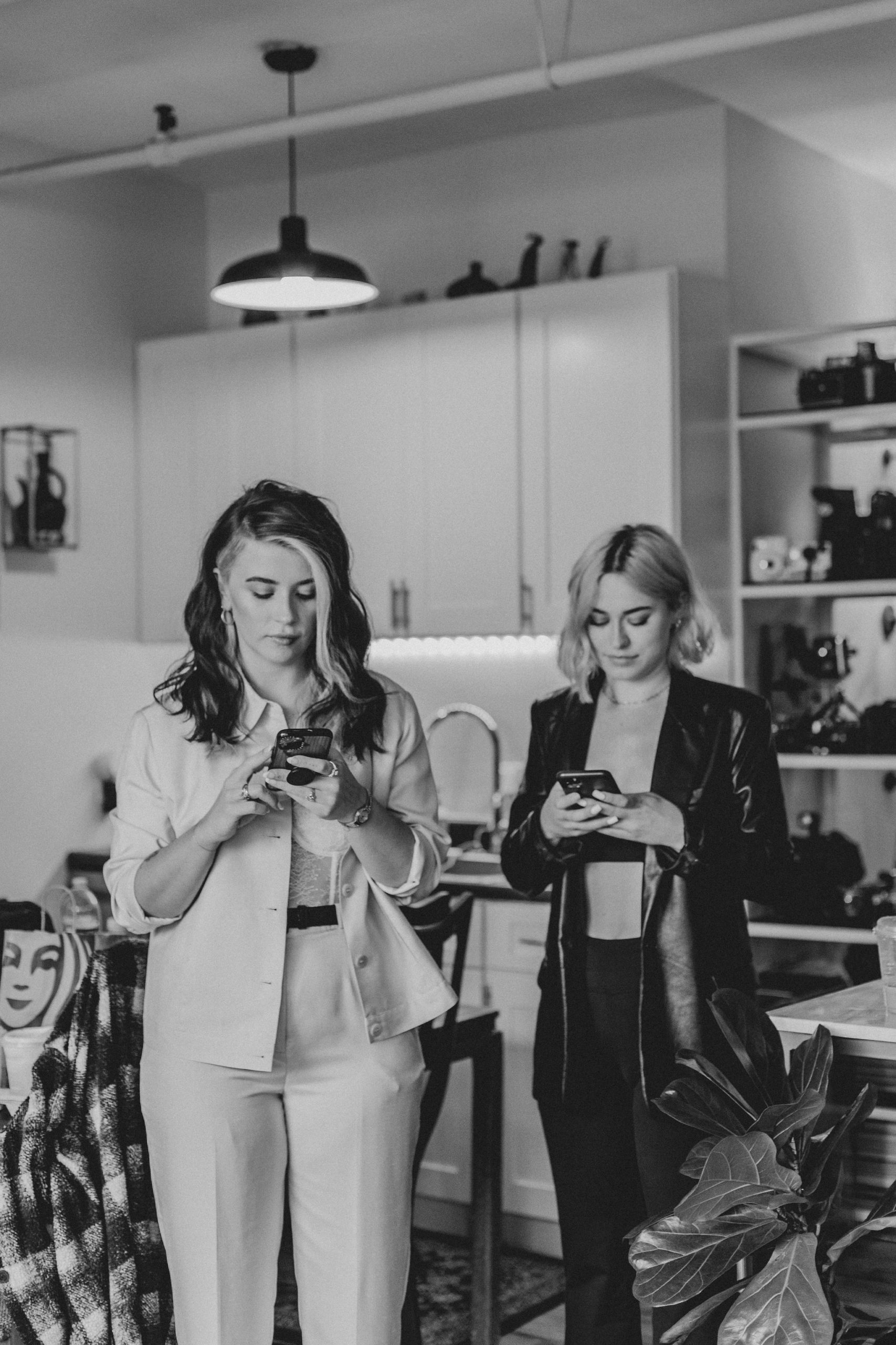 A black and white image of two women, who are virtual assistants, looking at their phones. One is blonde with short hair and the other is brunette with medium length hair.